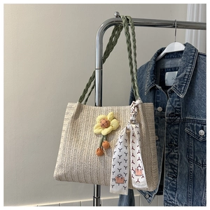 Detail of straw tote bag with green twisted handle and colorful floral ornaments