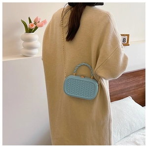 Detail of light blue crossbody bag with woven texture and gold chain worn by a model