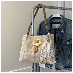 Detail of beige straw tote bag featuring yellow flower charm and decorative silk scarf