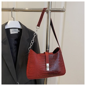 Detail of red-brown crocodile embossed handbag with silver square turn-lock and chain strap