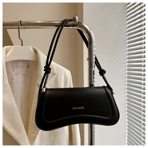Detail view of a black leather underarm bag with gold logo and knotted strap on a hanger