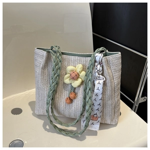 Close-up of woven tote bag featuring green braided handles and a decorative silk scarf