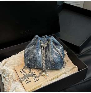 Detail of blue denim bucket bag featuring silver sequins and pearl chain strap in a gift box