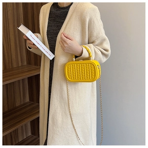 Detail of yellow embossed box bag with woven texture, top handle and gold chain strap