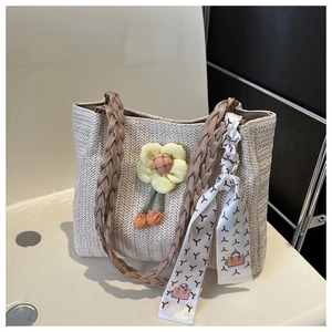 Close-up of beige straw tote bag with brown handles, floral charm and printed silk scarf