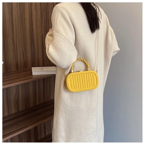 Detail of yellow embossed crossbody bag with braided texture and gold chain strap