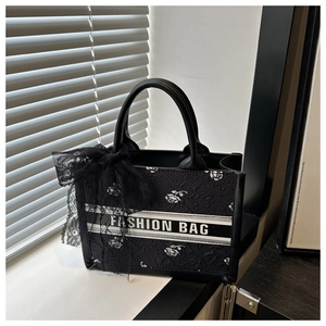 Close-up of black tote bag with white rose embroidery and a stylish lace bow detail