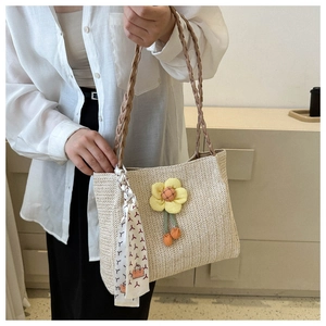 Detail of woven straw tote bag with yellow flower charm and silk scarf handle accent