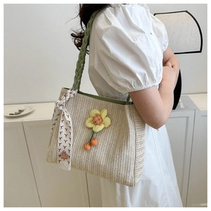 Detail of beige straw tote bag with sunflower decor, green handle, and printed silk scarf