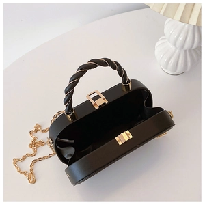 Detail of black box bag showing golden lock, braided handle and metal chain strap