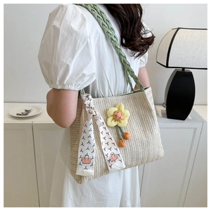 Detail of woven straw tote bag with green handles and decorative floral scarf accessory