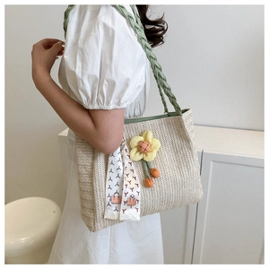 Close-up of woven straw tote bag featuring green straps and decorative yellow floral charm