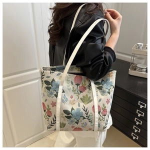 Detail view of a large tote bag featuring vintage floral embroidery and leather handles