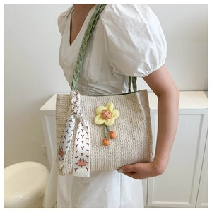 Detail of hand-woven straw tote bag featuring green handles and yellow fabric flower charm