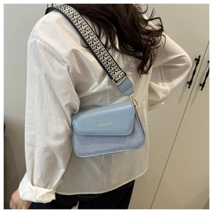 Detail of light blue crossbody bag with striped patchwork and wide geometric shoulder strap
