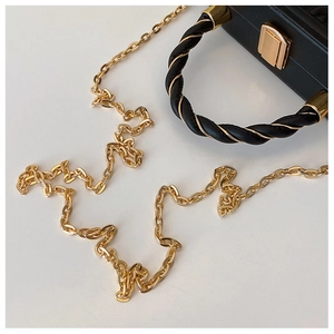 Close-up of black handbag with twisted gold handle and refined metal chain strap