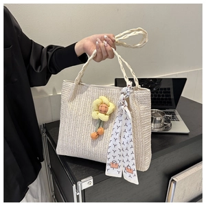 Close-up of beige woven straw tote bag with yellow floral charm and printed scarf
