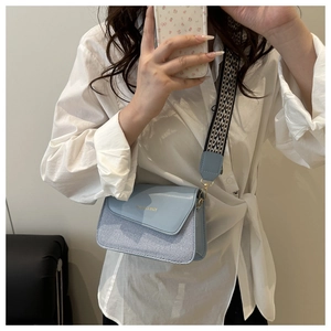 Detail of light blue crossbody bag with striped fabric and wide patterned strap on a model