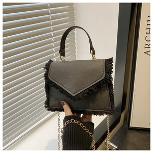 Détail d'un sac en cuir noir avec franges vintage et bandoulière chaîne dorée