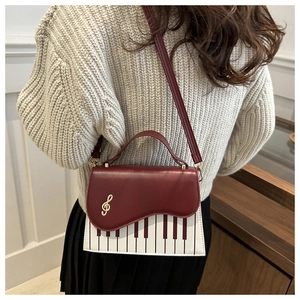 Detail of burgundy piano key shoulder bag with golden treble clef and wavy flap