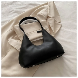 Detail of minimalist black leather crescent bag showing bottom metal studs on beige blazer