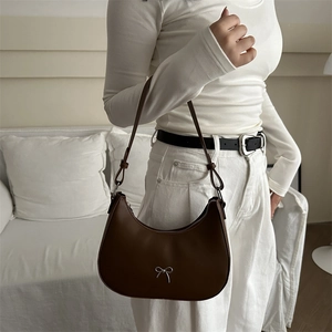 Brown faux leather hobo bag with silver bow buckle worn over the shoulder in a cozy setting