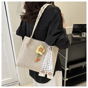 Detail of beige straw tote bag with floral charm and printed scarf handle on a model