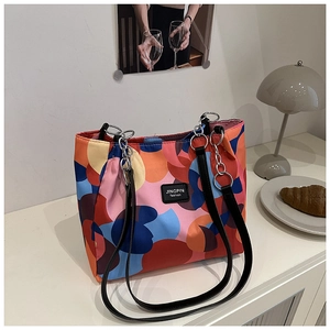 Detail view of colorful geometric patchwork tote bag with chain strap on white desk