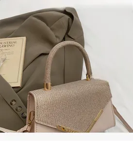 Close-up of beige handbag featuring metallic mesh cover and elegant V-shaped gold trim