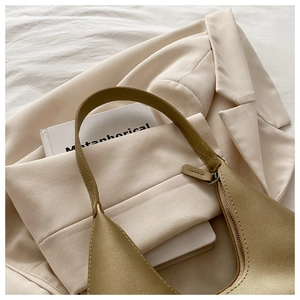 Close-up of golden matte faux leather underarm bag on stylish cream blazer background