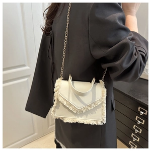 Détail d'un sac à franges blanc avec chaîne dorée, porté sur un blazer noir élégant
