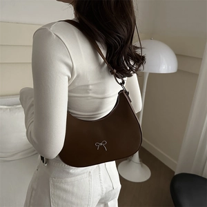 Deep brown leather crescent shoulder bag with silver bow accent worn by a model