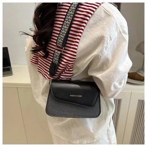 Close-up of woven fabric crossbody bag with wide jacquard strap and lettered flap
