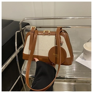 Detail of canvas and brown leather tote showing adjustable strap and gold zipper accents