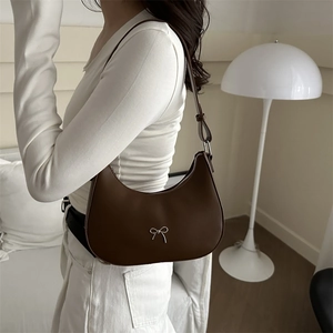 Detail of a dark brown crescent hobo bag with silver bow charm worn by a model