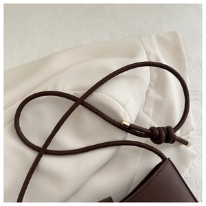 Detail of dark brown leather crossbody bag featuring knotted shoulder strap with gold caps