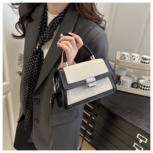 Détail d'un sac bandoulière tissé beige avec bordure en cuir noir et fermoir rotatif argent
