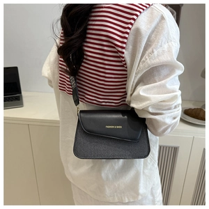 Detail of two-tone crossbody bag with wide strap and gold text, worn by model