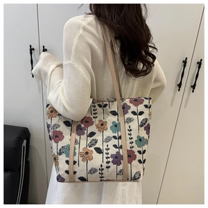 Detail of floral embroidery on a large beige fabric tote bag with leather handles