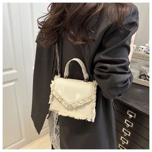 Détail du sac à main crème à franges avec chaîne dorée porté par un mannequin