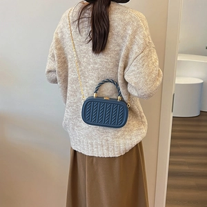 Navy blue embossed box bag with gold chain strap shown on a model in knitwear