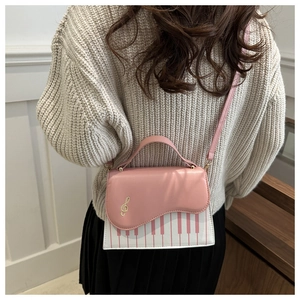 Detail of music-themed pink handbag featuring golden note ornament and piano key pattern