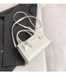 Detail of white bow handbag with metal buckle on a grey blazer background