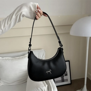 Detail of black moon-shaped hobo bag featuring a decorative silver metal bow and adjustable strap