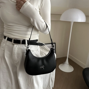Detail of black faux leather crescent bag featuring a silver metal bow and slim strap