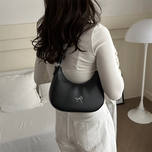 Detail of black hobo bag with silver bow accent worn by model in a minimalist room