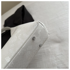 Detail shot of white snakeskin texture handbag featuring silver protective base rivets