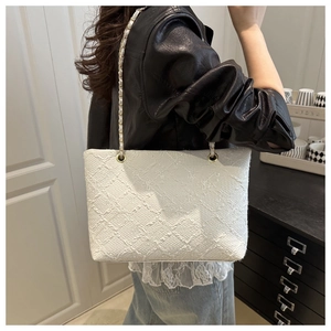 Gros plan d'un sac cabas en tweed blanc avec broderies matelassées et détails de chaîne dorée