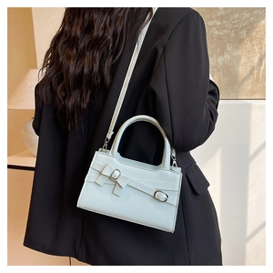 Close-up of a light blue glossy leather square bag featuring a stylish bow and metallic buckle