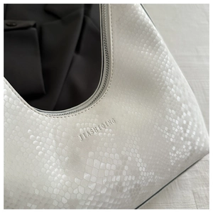 Close-up of white snakeskin texture and embossed brand logo on the trendy handbag